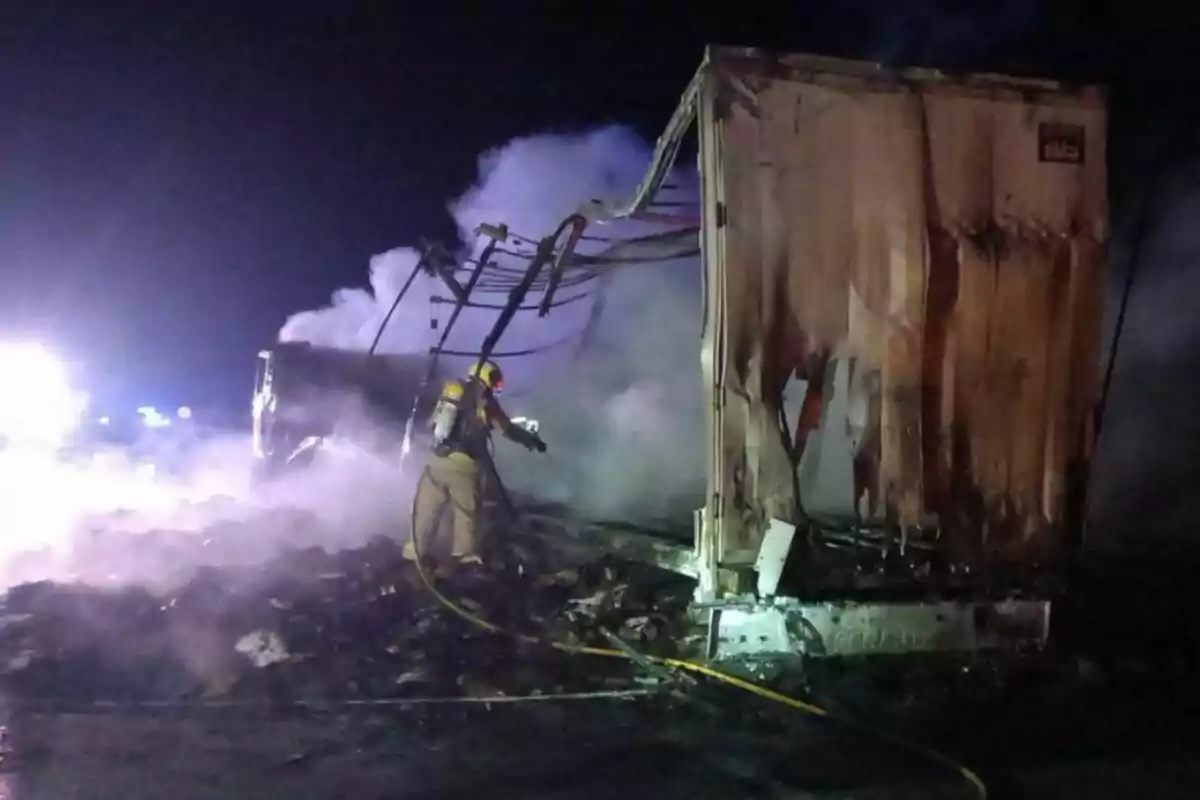 Bomber apagant un incendi en un camió a la nit, amb fum dens al voltant.