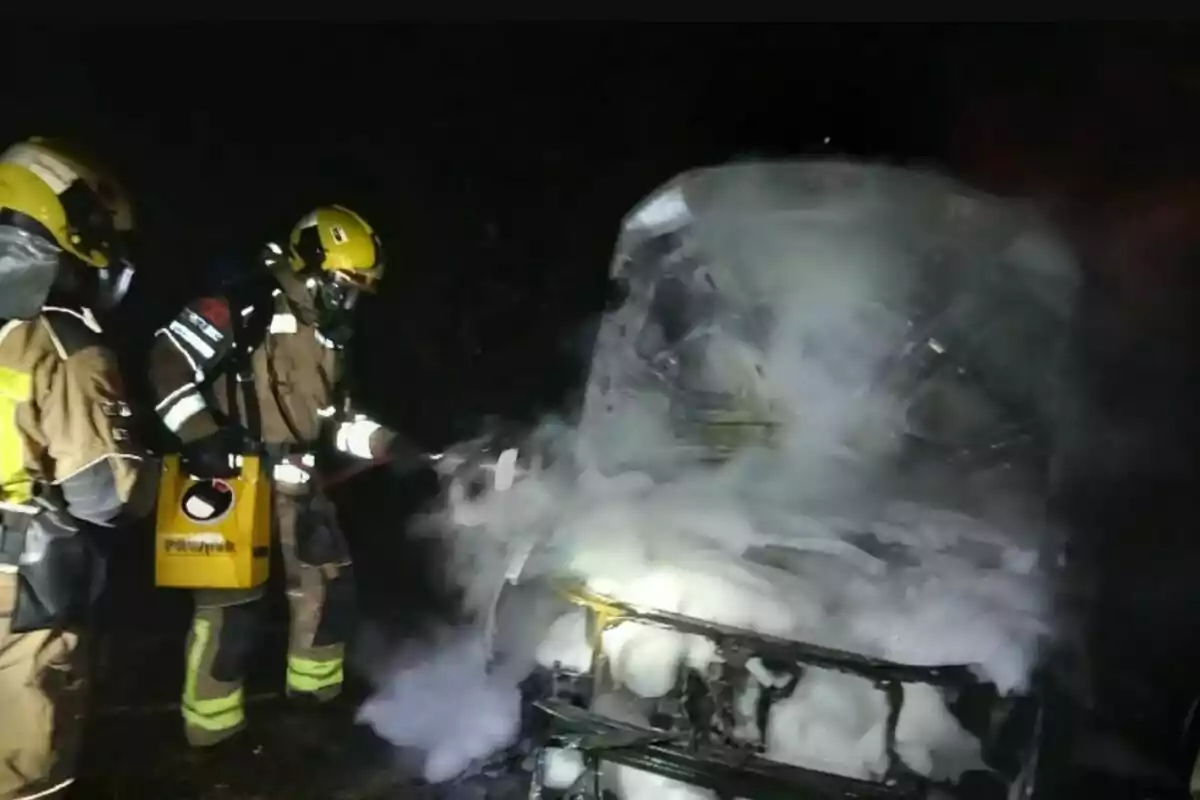 Bomberos apagando un incendio en un vehículo con espuma en la oscuridad.