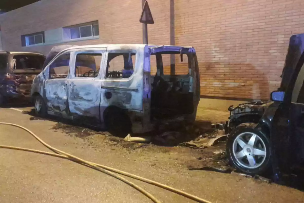 Una furgoneta quemada estacionada en la calle junto a otros vehículos dañados por el fuego.