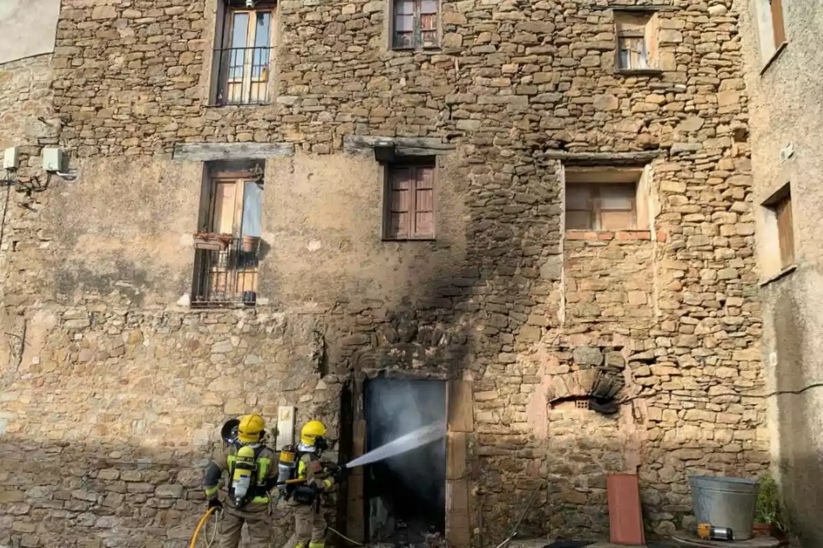 Bomberos con equipo de protección apagan un incendio en la entrada de un edificio de piedra.