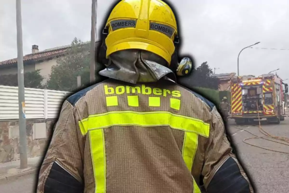 Bombarder d’esquena amb casc groc i jaqueta reflectant en un carrer on hi ha un camió de bombers i mànegues desplegades