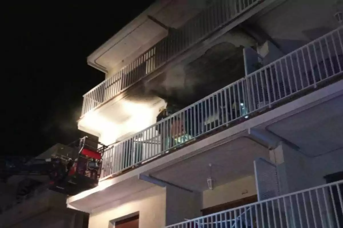 Un edificio de apartamentos con un balcón en llamas durante la noche mientras un camión de bomberos se encuentra en la escena.