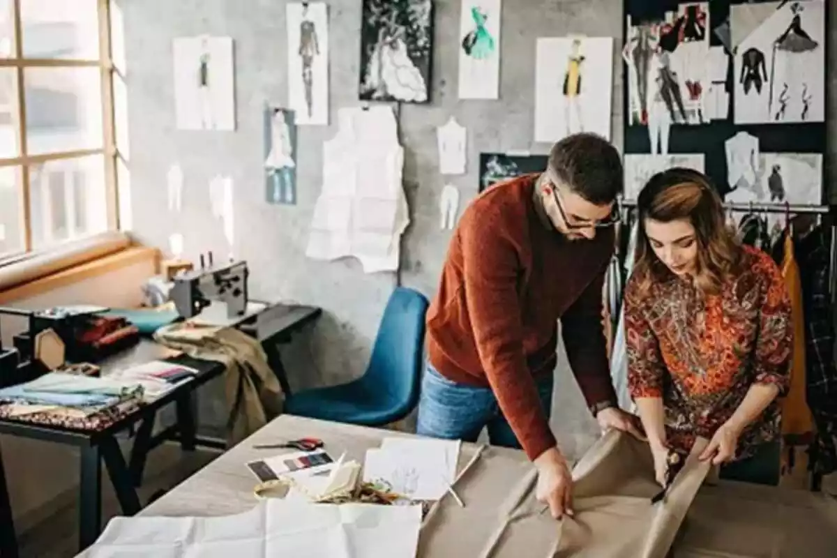 Un home i una dona joves en un taller de costura tallant una tela