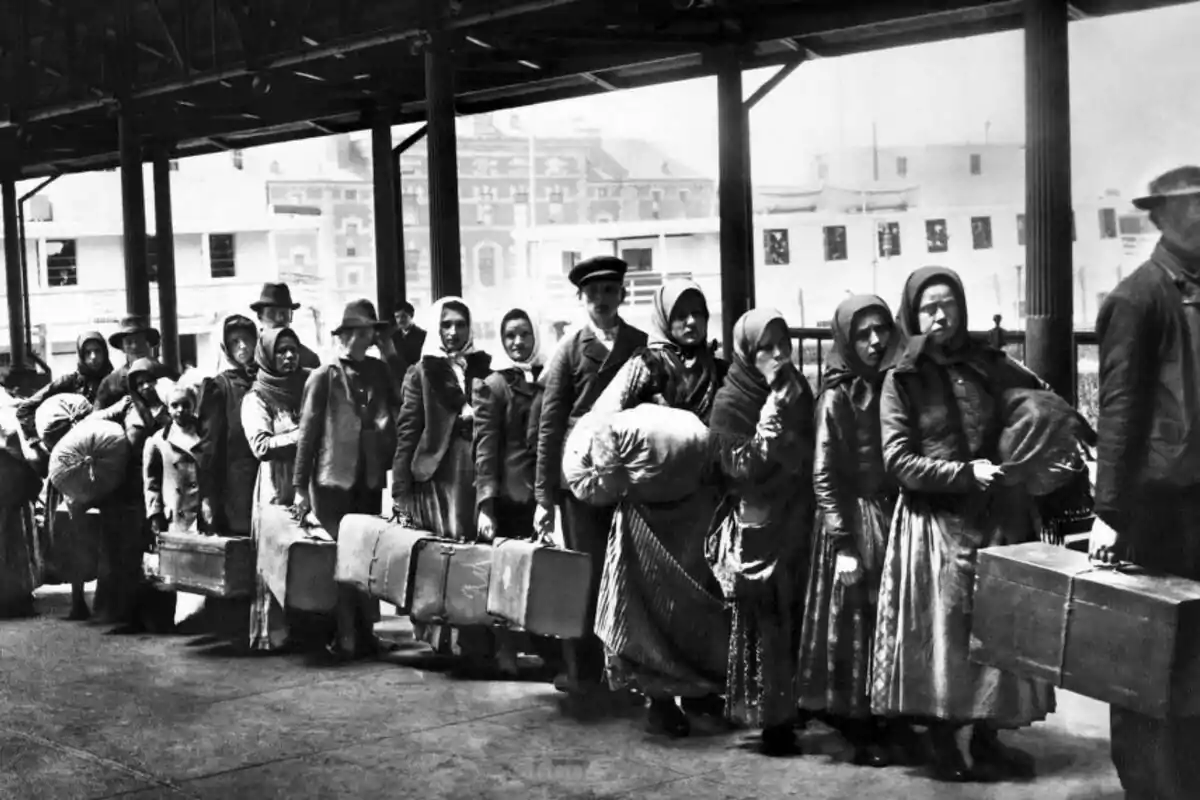 Un grup de persones amb roba dèpoca i equipatge, fent fila en una estació o port.