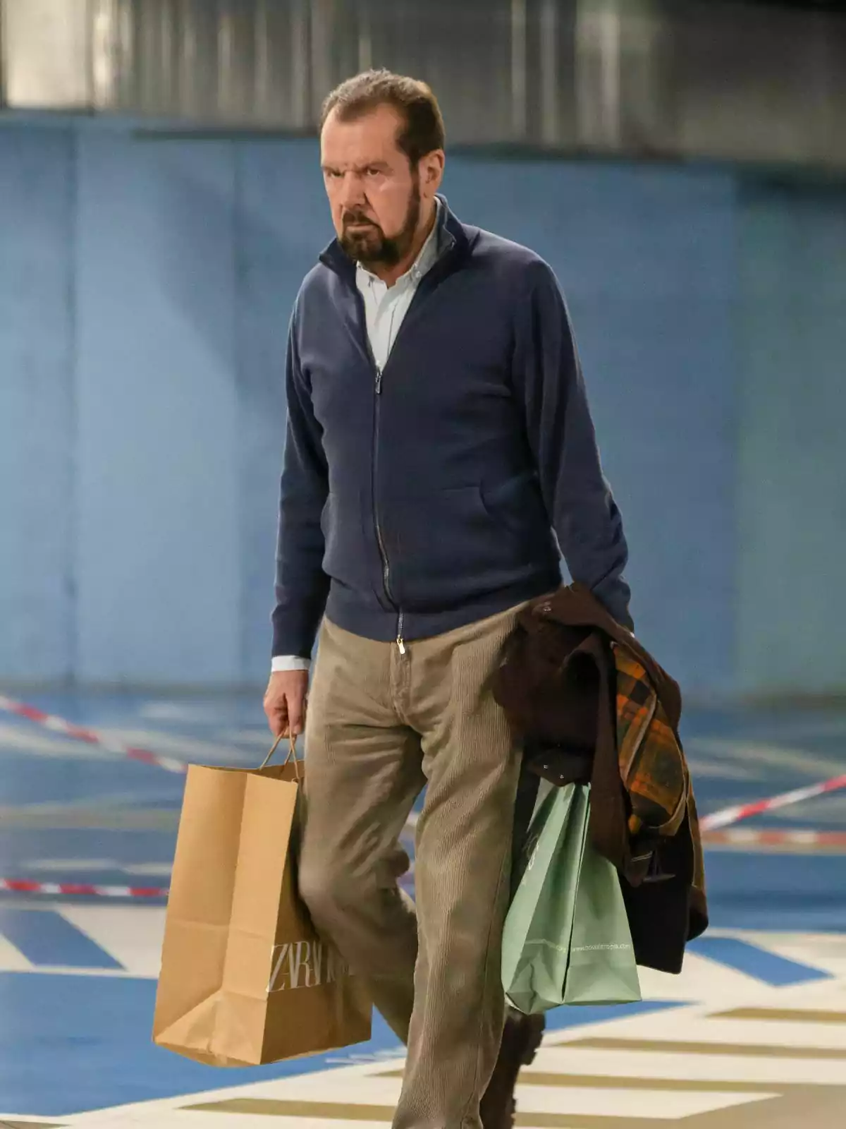 Jesús Ortiz with a beard and short hair carries shopping bags and a coat in a parking lot. Jesús Ortiz with a beard and short hair carries shopping bags and a coat in a parking lot.