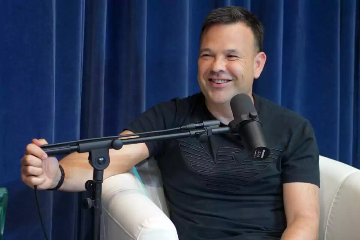 Hombre sonriendo mientras habla en un micrófono durante una entrevista.