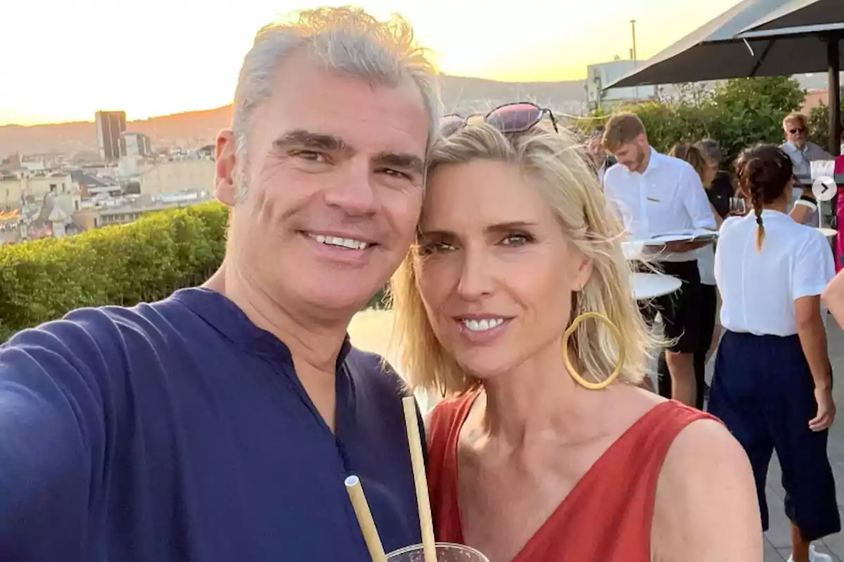 Una pareja sonriente toma una selfie al atardecer en una terraza con vista a la ciudad.