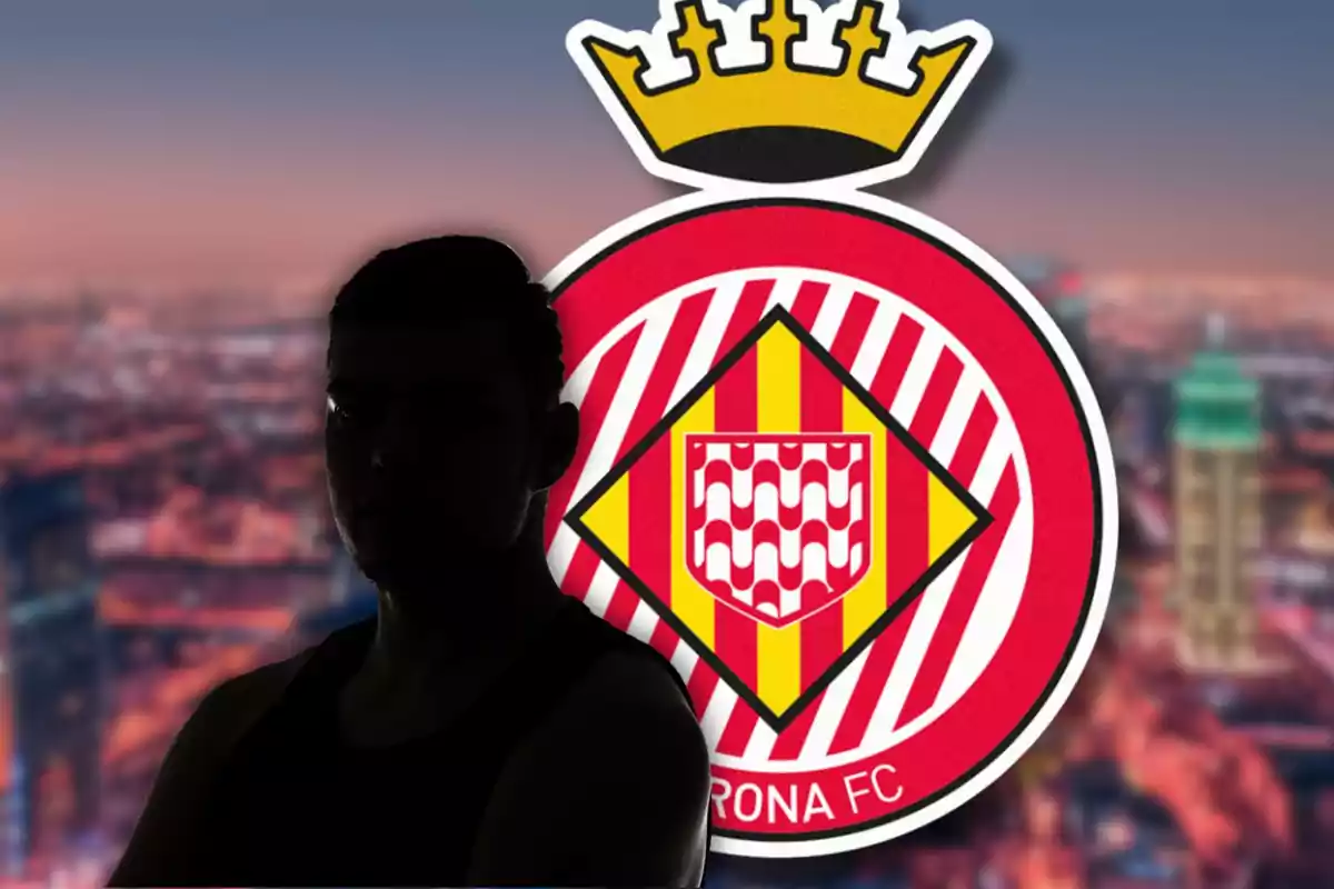 Una persona en silueta davant de l'escut del Girona FC amb un fons urbà desenfocat cap al tard.