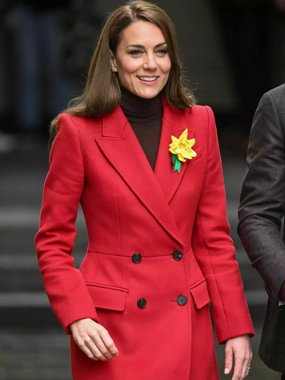 Kate Middleton con un abrigo rojo y un broche de flor amarilla sonríe mientras camina. Kate Middleton con un abrigo rojo y un broche de flor amarilla sonríe mientras camina.