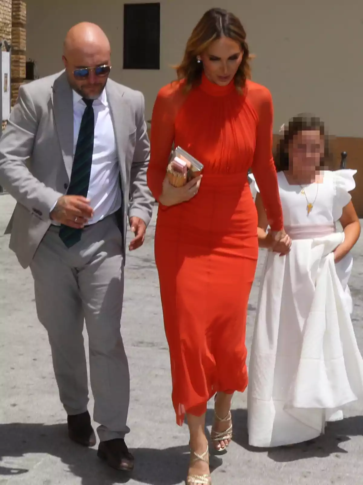 Kiko Rivera amb vestit gris i corbata, Irene Rosales amb vestit vermell i sandàlies daurades i una nena vestida de blanc caminen junts a l’aire lliure. Kiko Rivera amb vestit gris i corbata, Irene Rosales amb vestit vermell i sandàlies daurades i una nena vestida de blanc caminen junts a l’aire lliure.
