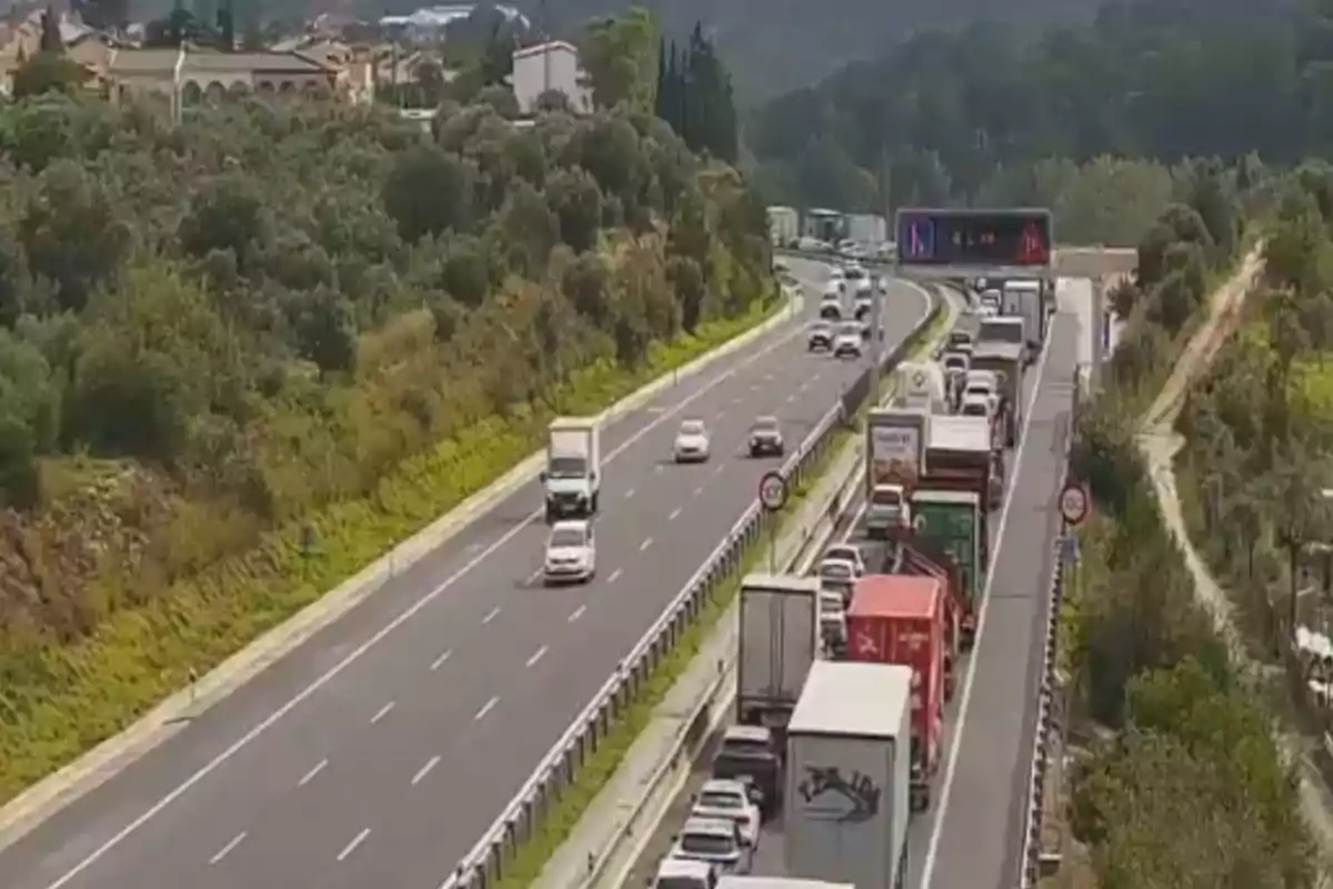 Carretera con tráfico denso en un carril y flujo libre en el otro rodeada de vegetación y casas al fondo.