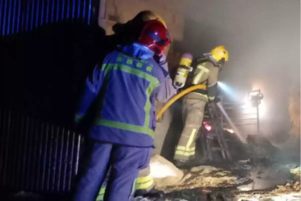 Bomberos trabajando en la extinción de un incendio en un edificio con humo denso y equipo de protección.