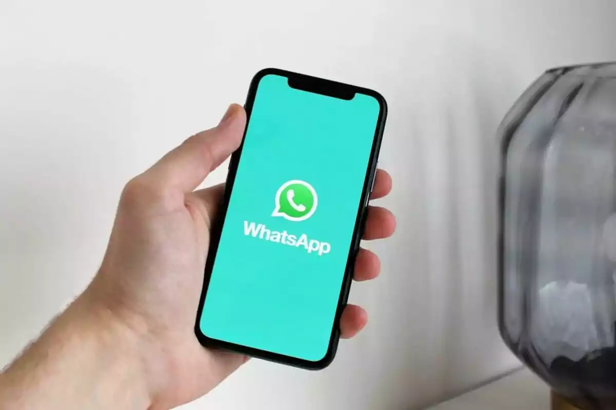 Una mano sosteniendo un teléfono móvil con la pantalla de inicio de WhatsApp.