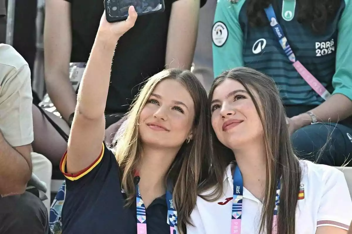 Dos joves es prenen una selfie mentre assisteixen a un esdeveniment esportiu, totes dues porten penjades acreditacions i una vesteix una samarreta amb els colors de la bandera d'Espanya.