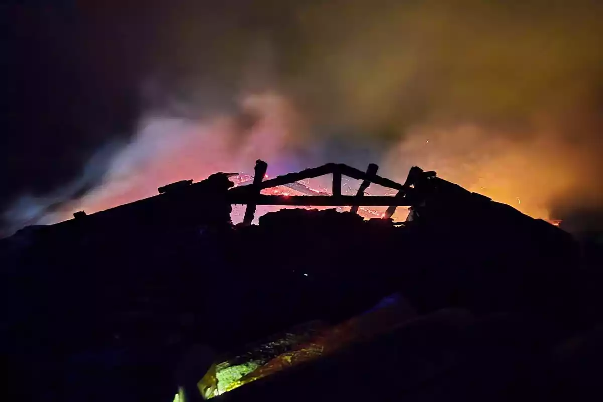 Estructura en silueta contra un fondo de llamas y humo en la noche.