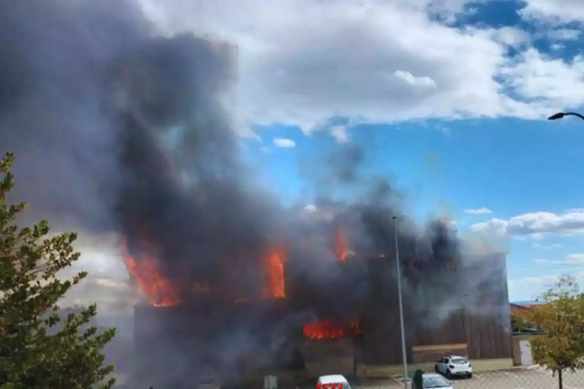 Edifici en flames amb una gran quantitat de fum negre sota un cel parcialment ennuvolat.