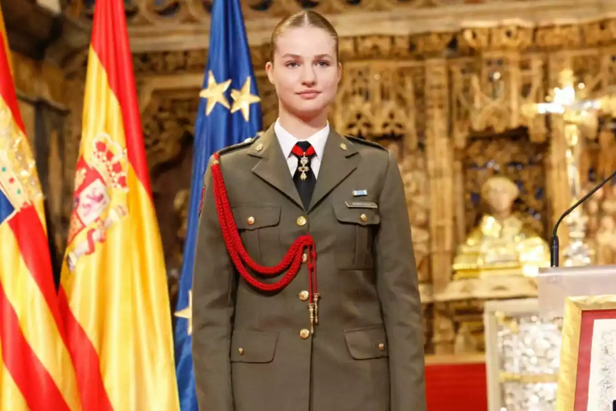 Una noia vestida amb uniforme militar es troba dreta davant de les banderes d'Espanya i la Unió Europea en un entorn decorat amb detalls daurats.