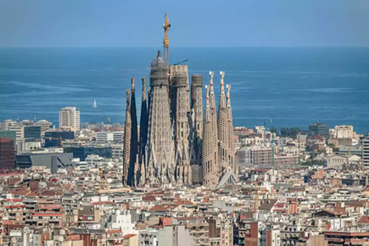 Vista aèria duna ciutat amb una catedral en construcció i el mar al fons.