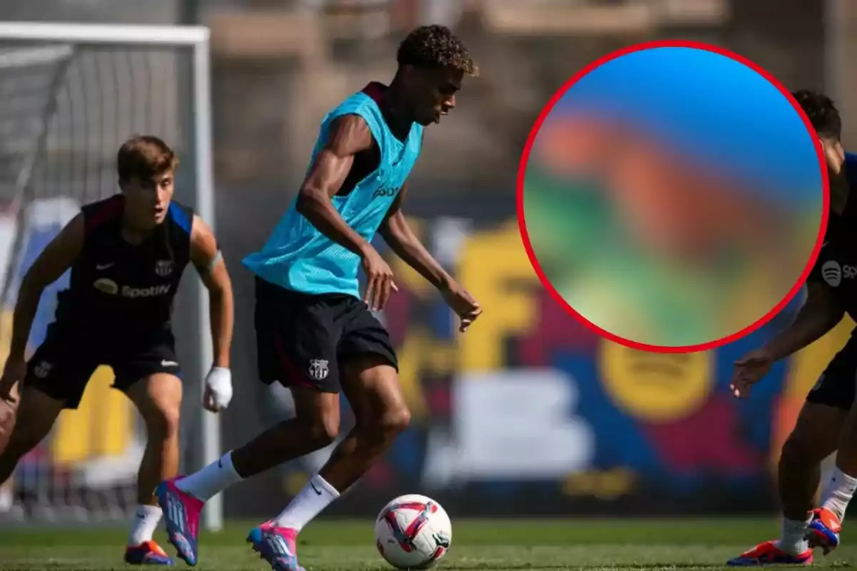 Jugadors de futbol entrenant en un camp, un porta un peto blau i està controlant la pilota mentre dos jugadors més observen.