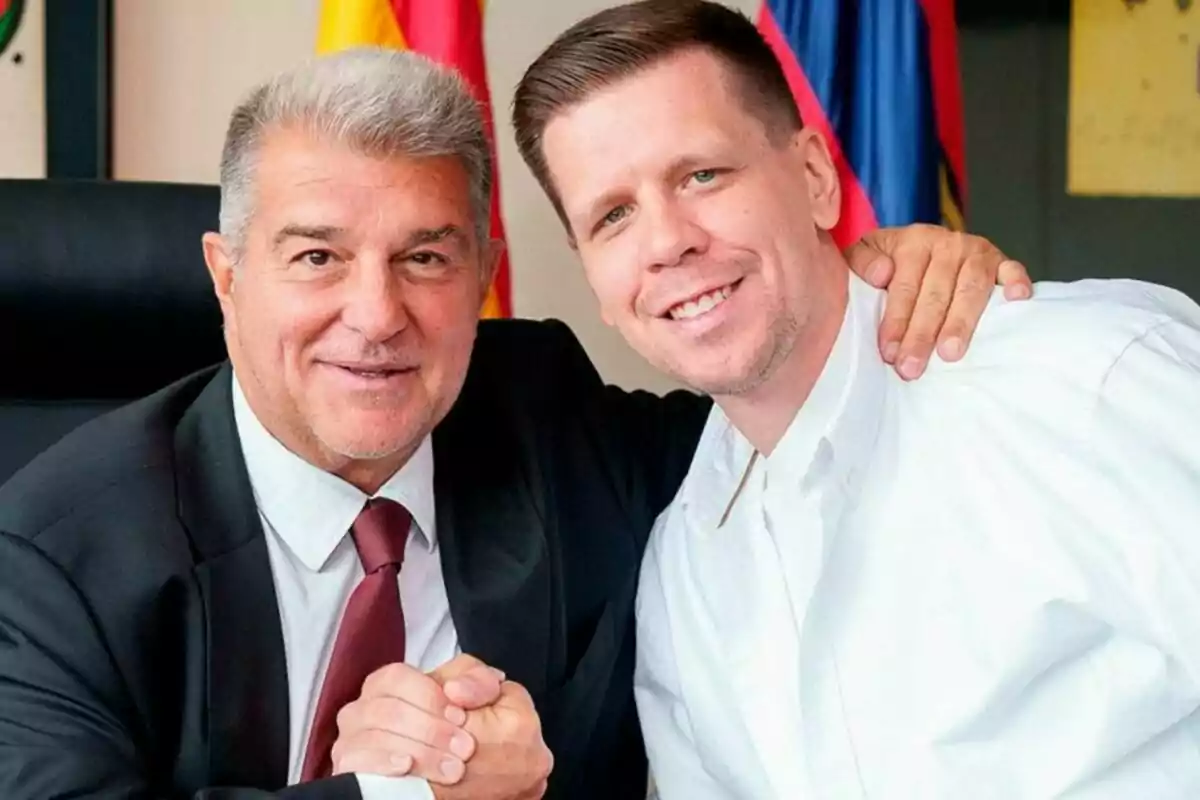 Dos homes somrients posen junts mentre es donen la mà, un porta vestit i corbata i l'altre vesteix camisa blanca.