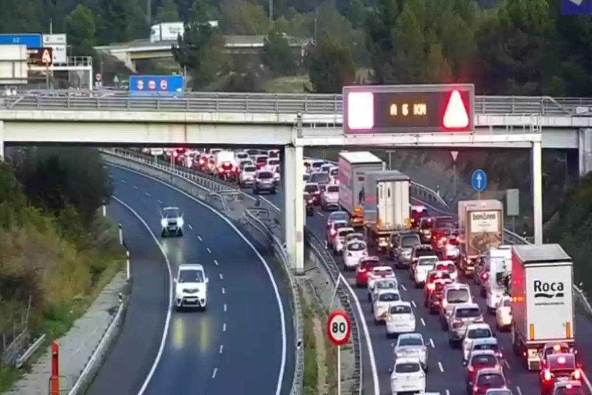 Una carretera con tráfico denso en un carril mientras el otro está despejado, con un puente y señales de tráfico visibles.