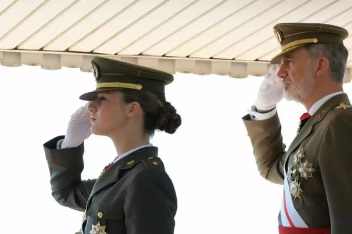 Dos personas en uniforme militar saludando con la mano derecha bajo un techo.