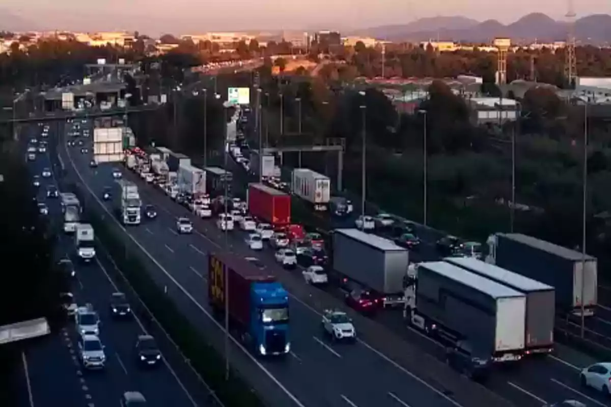 Tráfico denso en una autopista con varios camiones y coches en ambos sentidos durante el atardecer.