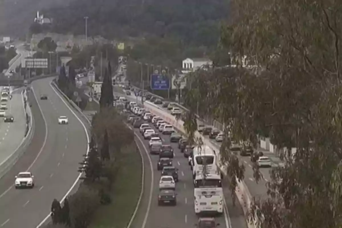 Una carretera con tráfico denso en un carril y flujo libre en el otro rodeada de árboles y colinas.