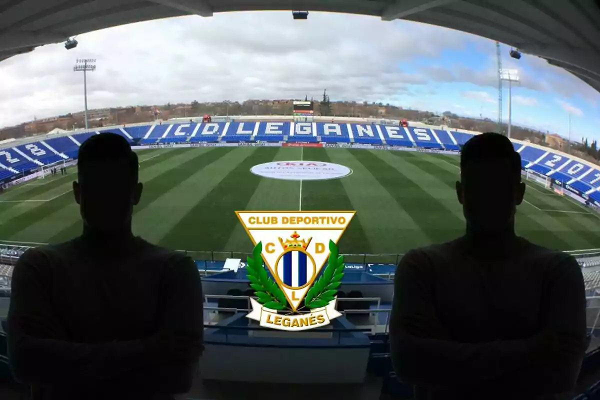 Vista de l'estadi del Club Esportiu Leganés amb dues siluetes de persones a primer pla i l'escut de l'equip al centre.