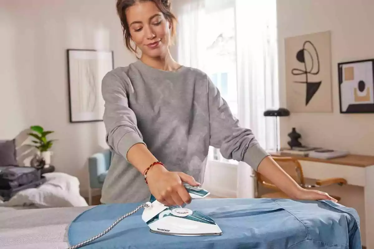 A woman ironing a blue shirt in a well-lit room with modern decor. A woman ironing a blue shirt in a well-lit room with modern decor.