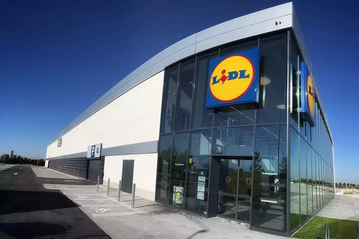 Lidl gran, d'extraradi, amb parets de vidre per la part de la botiga i, a l'esquerra, l'entrada al pàrquing subterrani amb paret de formigó.