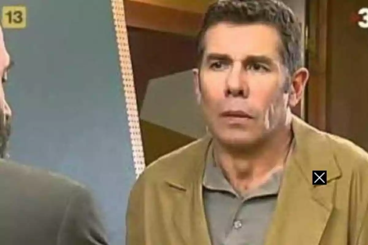 Hombre con expresión seria usando chaqueta beige y camisa gris en un ambiente interior Hombre con expresión seria usando chaqueta beige y camisa gris en un ambiente interior