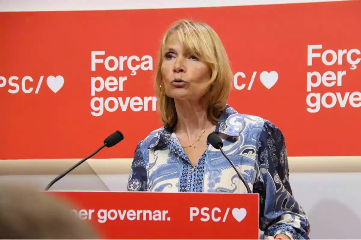 Dona parlant en un podi amb un fons vermell que diu “Força per governar” i “PSC/♥”.