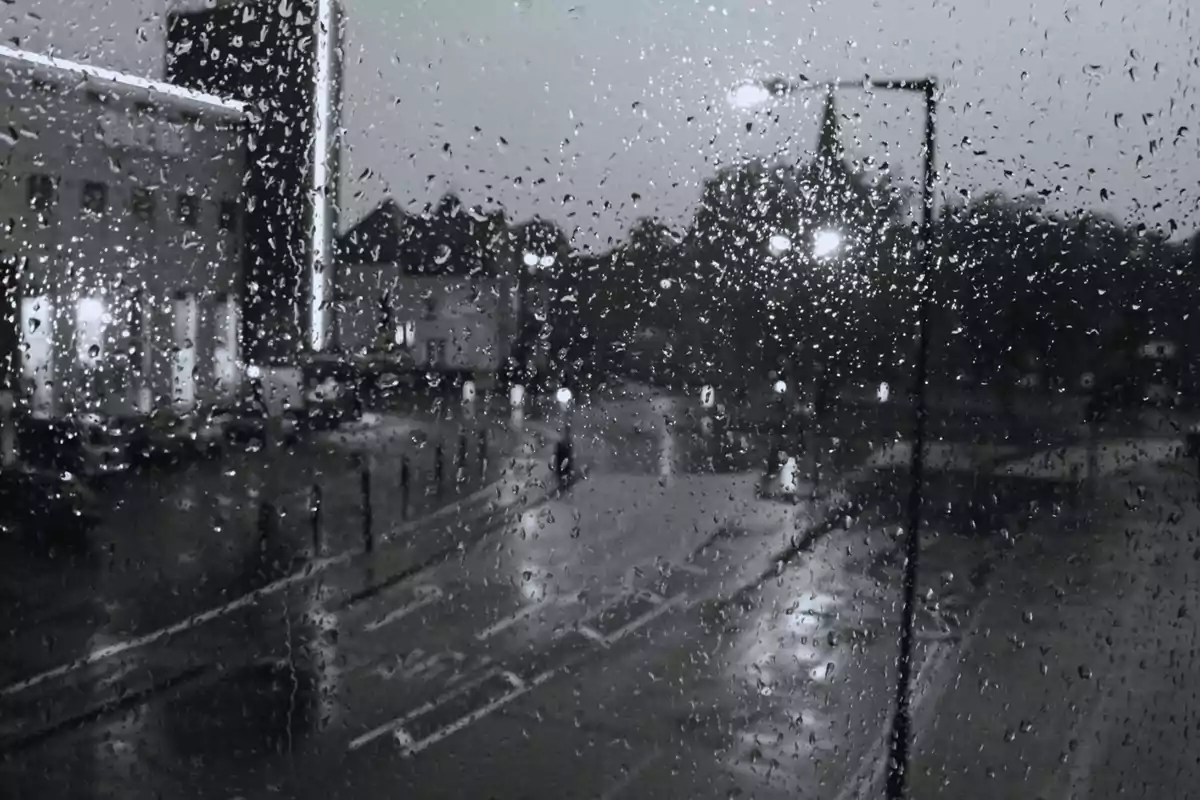 Vista de una calle lluviosa a través de una ventana con gotas de agua.