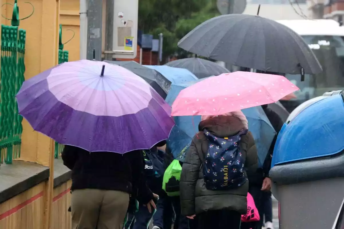 Imatge de diverses persones caminant sota la pluja amb un paraigua