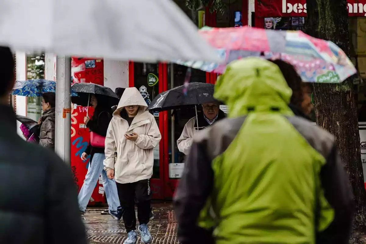 Persones es protegeixen de la pluja amb paraigües Persones es protegeixen de la pluja amb paraigües