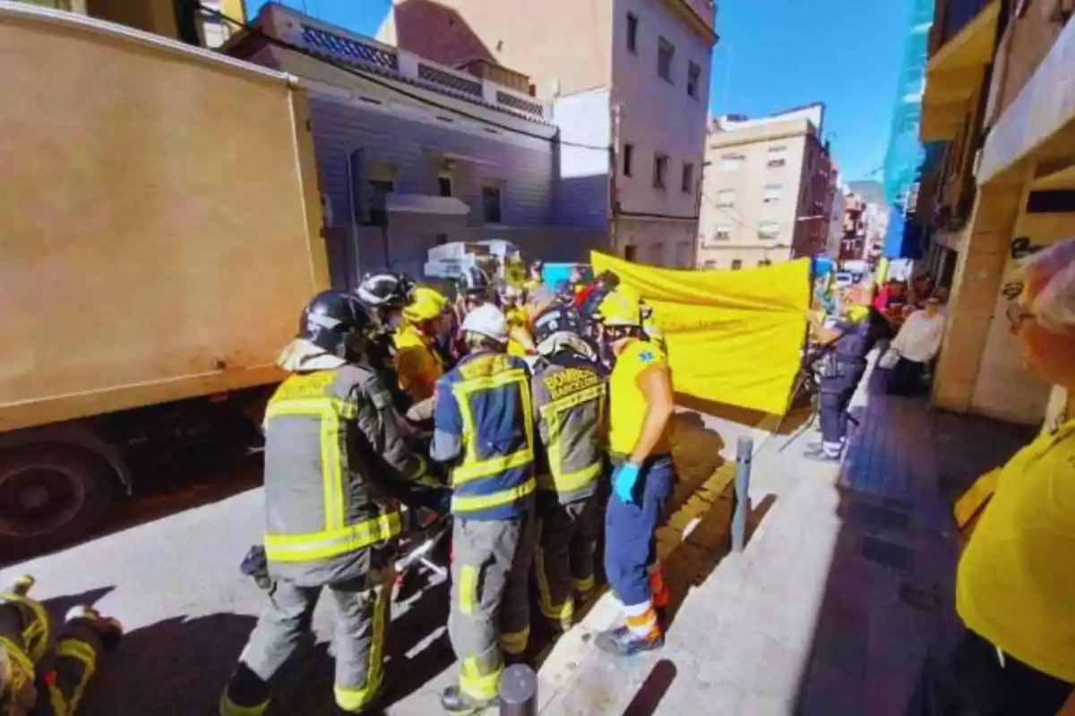 Bombers i personal d'emergència treballant en un carrer amb un camió, amb un grup de persones observant.