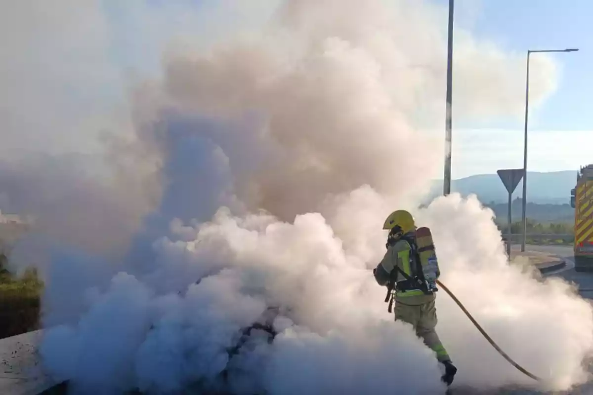 Bombero combatiendo un incendio en una carretera rodeado de humo blanco.