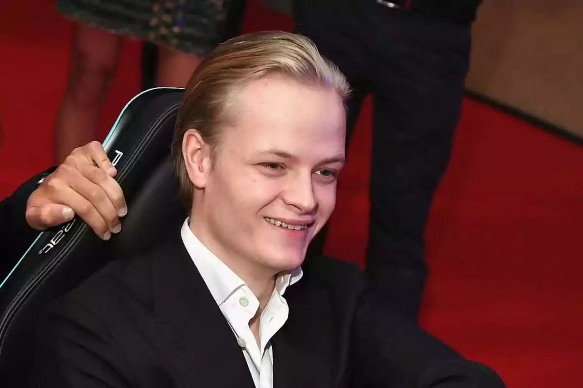 Marius Borg pentinat enrere, vestit amb una camisa blanca i un sac fosc, somrient mentre està assegut en una cadira amb un fons vermell. Marius Borg pentinat enrere, vestit amb una camisa blanca i un sac fosc, somrient mentre està assegut en una cadira amb un fons vermell.