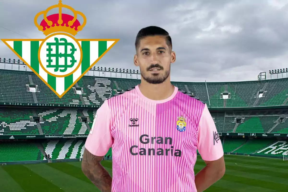 Un jugador de futbol amb una samarreta rosa de Gran Canària està dreta en un estadi de futbol amb el logotip del Real Betis al fons.