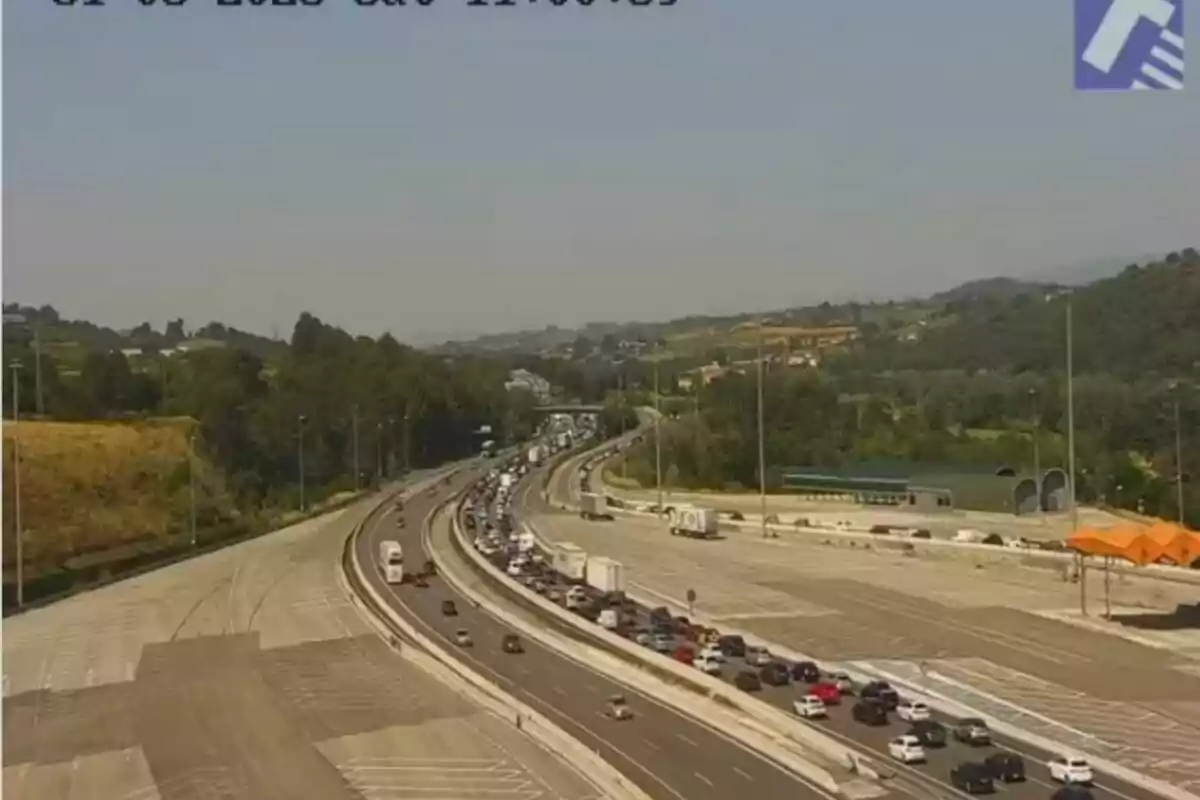 Trànsit dens en una autopista envoltada de zones verdes i turons sota un cel serè