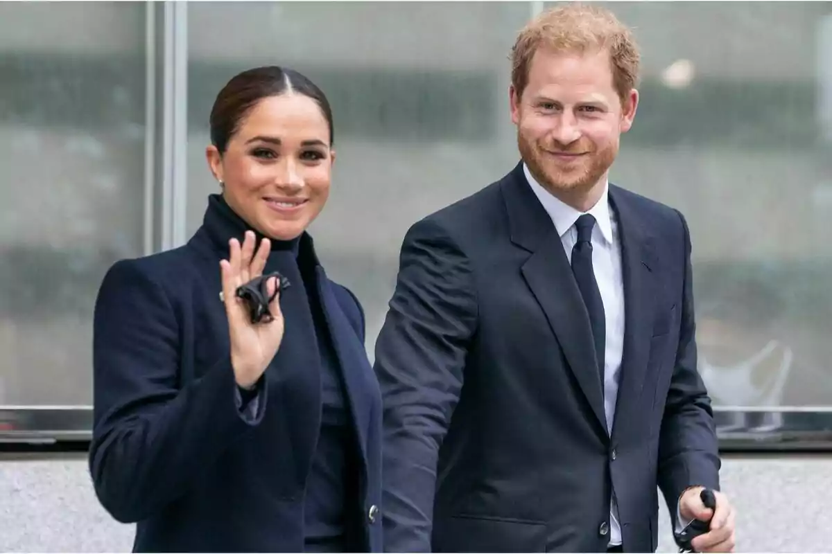 A woman and a man dressed elegantly smile as they walk together, the woman waves her hand.