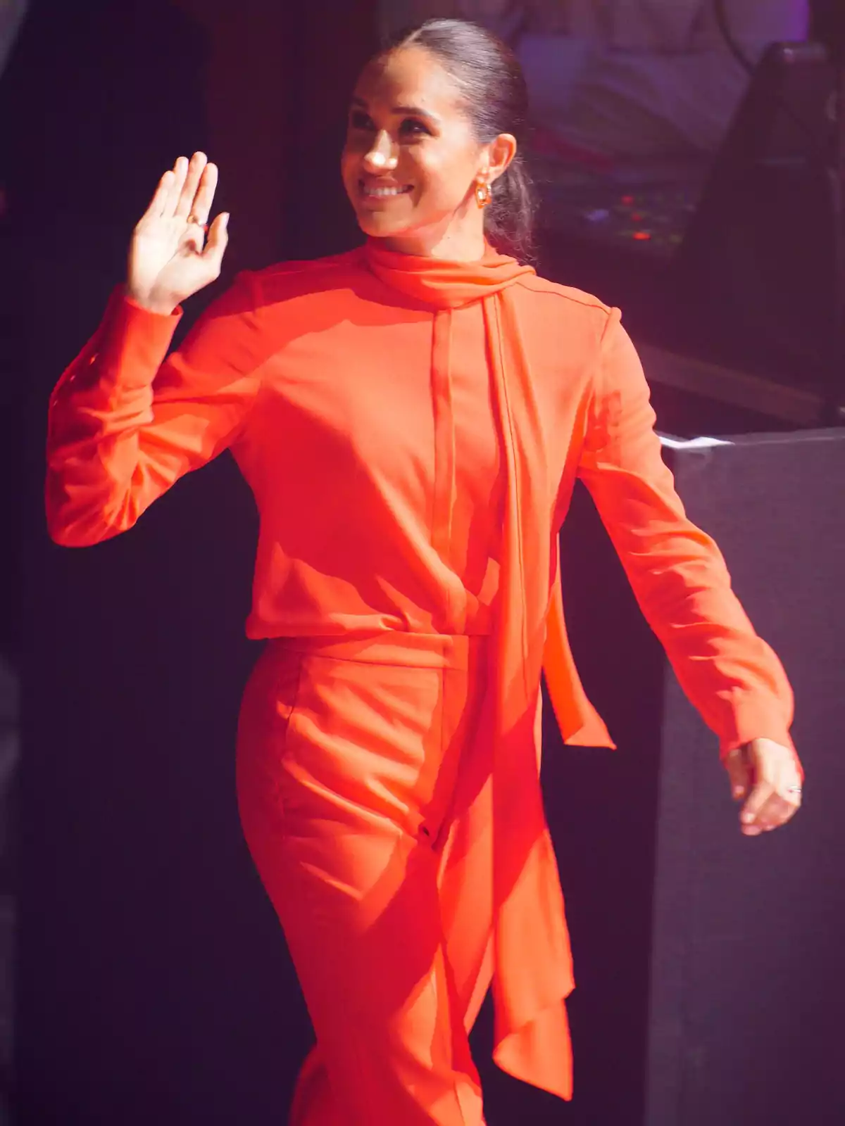 Meghan Markle amb un conjunt vermell brillant somriu i saluda mentre camina. Meghan Markle amb un conjunt vermell brillant somriu i saluda mentre camina.