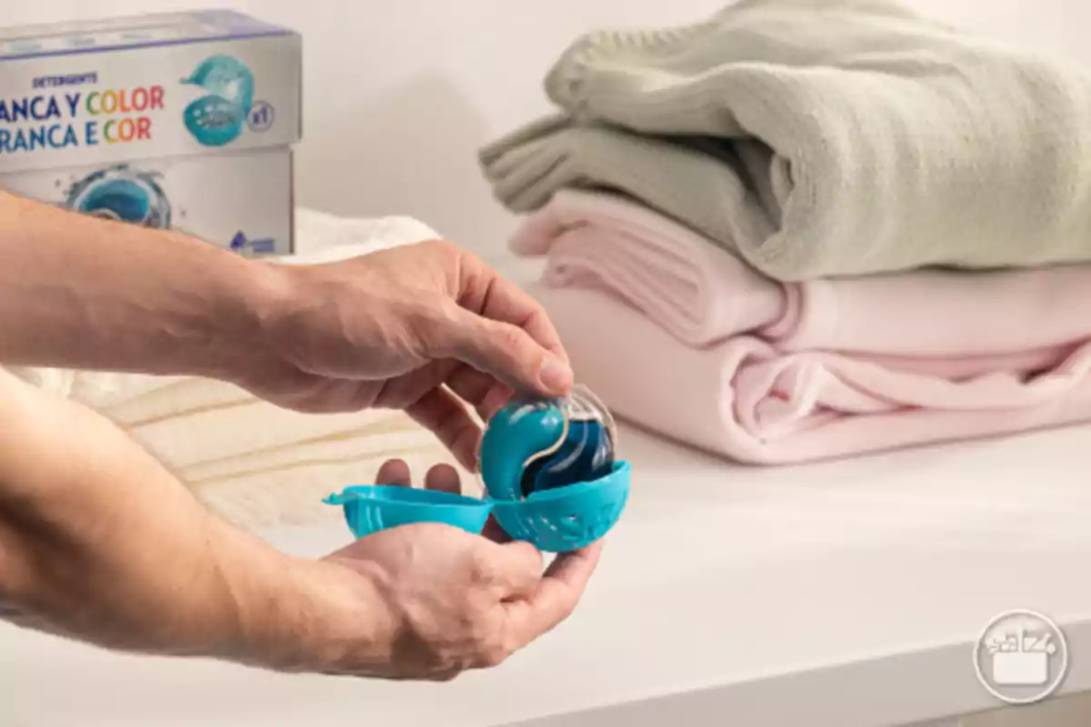 Persona sostenint una càpsula de detergent davant d'una pila de roba doblegada. Persona sostenint una càpsula de detergent davant d'una pila de roba doblegada.