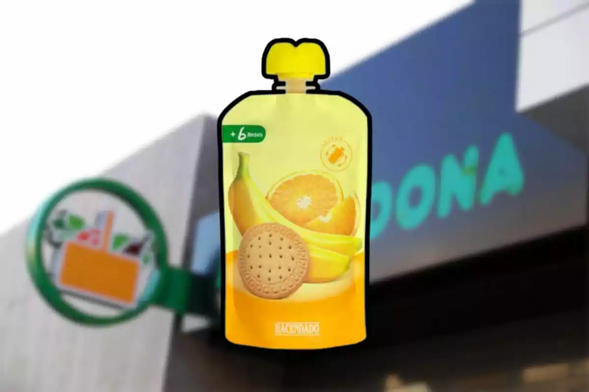 Un envàs de puré de fruites per a nadons amb imatges de plàtan, taronja i galeta davant d'un fons desenfocat d'un supermercat. Un envàs de puré de fruites per a nadons amb imatges de plàtan, taronja i galeta davant d'un fons desenfocat d'un supermercat.