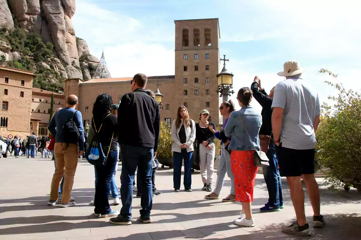 Un grup de persones en una visita guiada a un lloc històric amb edificis antics i muntanyes de fons.