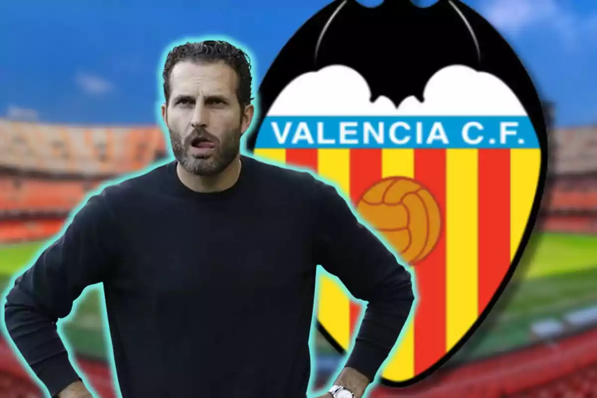 Hombre con barba y suéter negro frente al escudo del Valencia C.F. en un estadio.