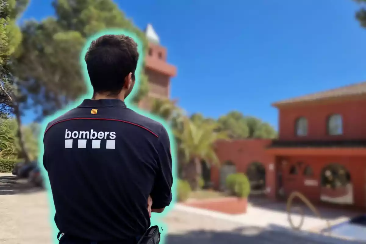 Un bomber d'esquena amb un uniforme que diu bombers en un entorn exterior amb edificis i arbres.