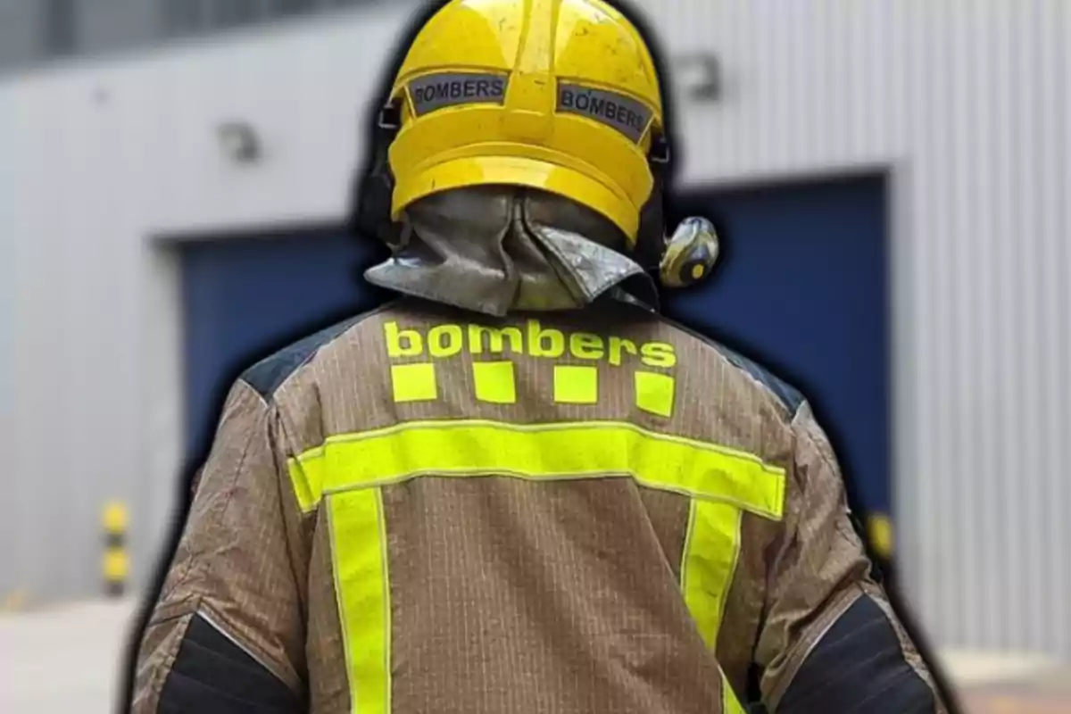 Bombero de espaldas con uniforme y casco amarillo frente a un edificio industrial.