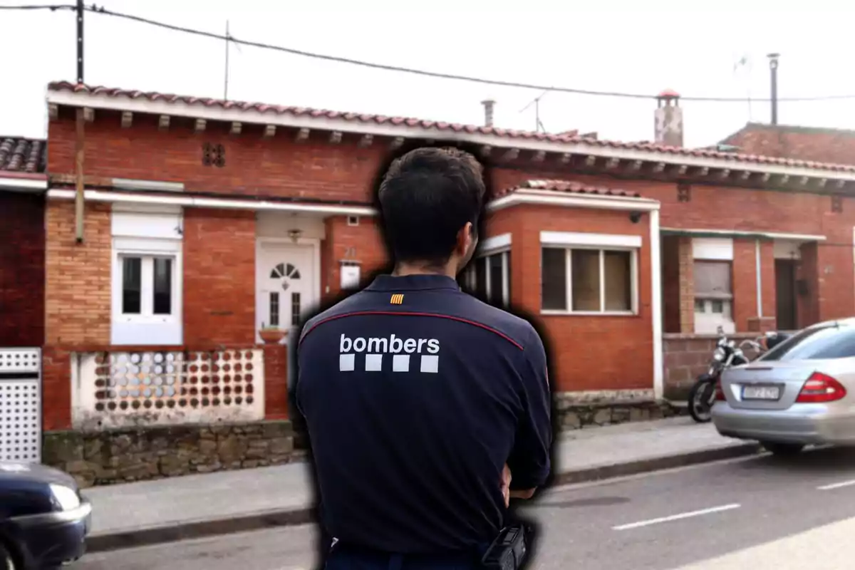 Un bomber d'esquena davant d'una casa de maó vermell.